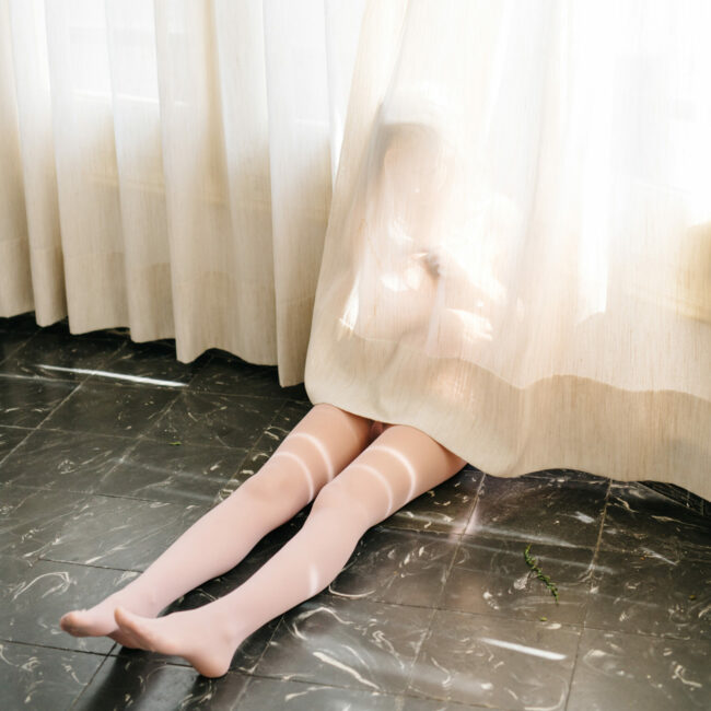 Unrecognizable attractive woman sitting and posing in drapes at window.